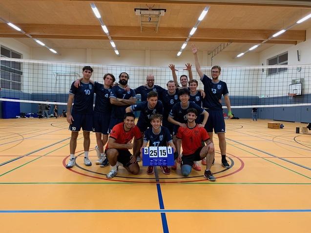 Eine Volleyballmannschaft posiert in einer Halle vor einem Netz, mit einem Punktestand von 3:1 und lächelndem Gesichtsausdruck.