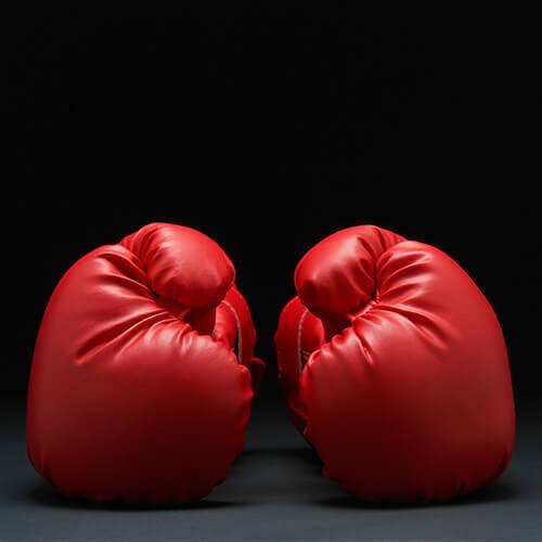 Zwei rote Boxhandschuhe stehen sich gegenüber vor einem schwarzen Hintergrund.