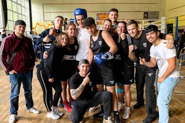 Eine Gruppe von insgesamt zehn jungen Menschen in Sportkleidung posiert gemeinsam in einer Boxhalle.
