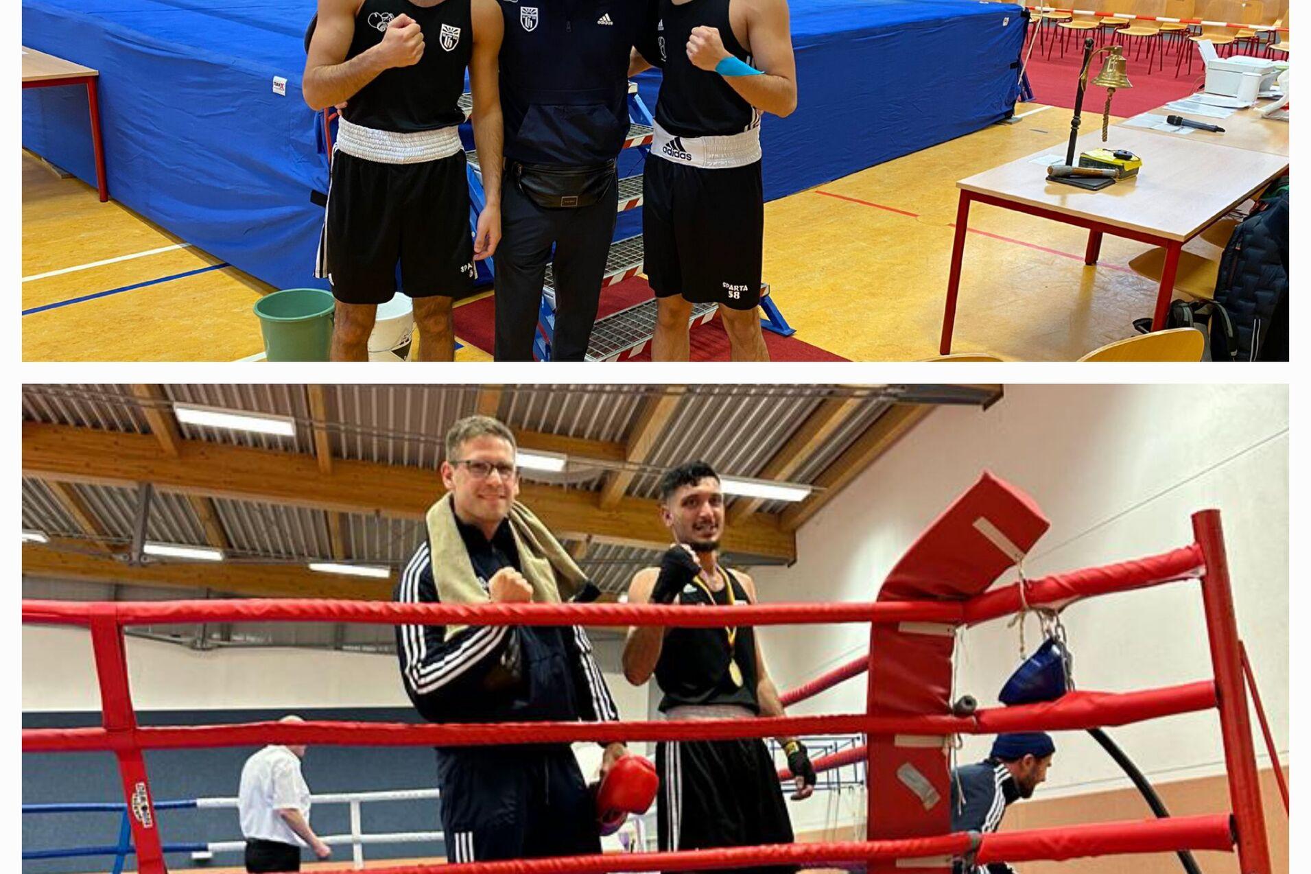 Drei Boxer posieren mit Trainer in einer Sporthalle neben einem Boxring und Tisch, während Zuschauer im Hintergrund sitzen.