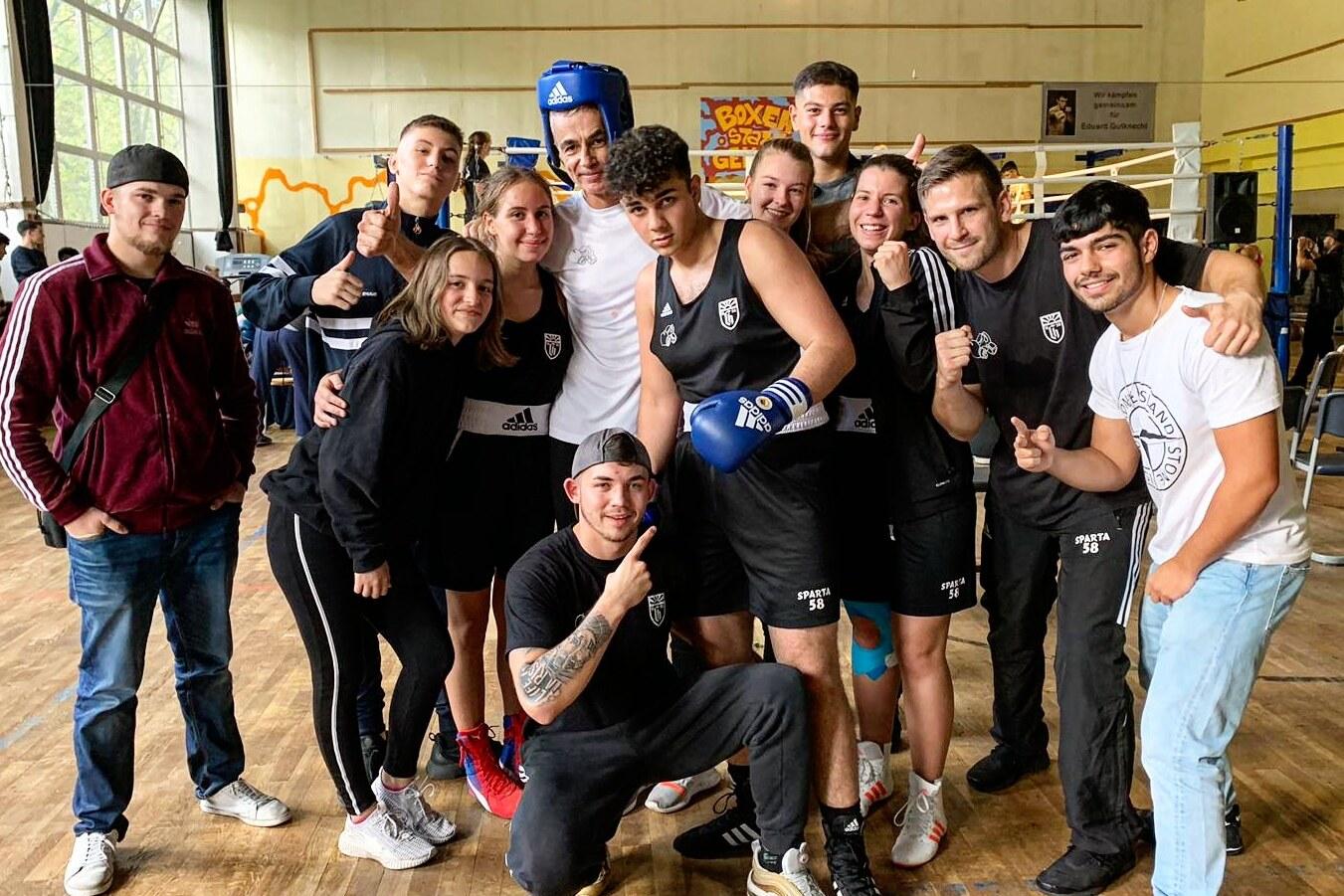 Eine Gruppe von insgesamt zehn jungen Menschen in Sportkleidung posiert gemeinsam in einer Boxhalle.