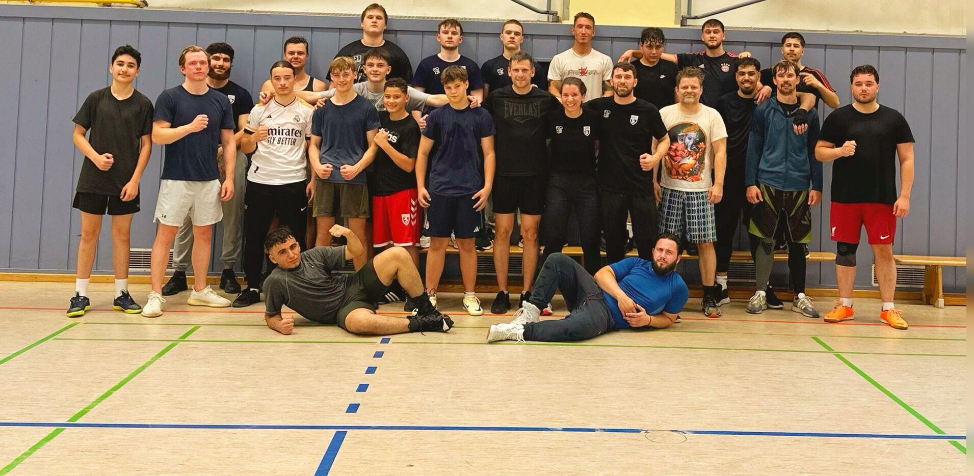 Gruppe von 20 Jugendlichen und jungen Erwachsenen posiert in Sportkleidung in einer Turnhalle nach dem Training.