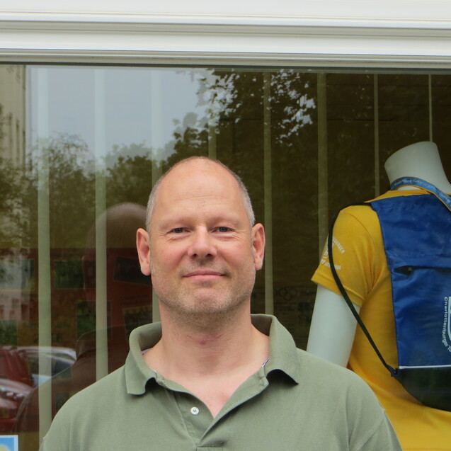 Mann mit kurzem Haar steht vor einem Schaufenster, in dem Sportbekleidung ausgestellt ist.