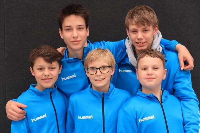 Fünf Jugendliche in blauen Hummel-Jacken stehen posierend vor einem grauen Hintergrund.