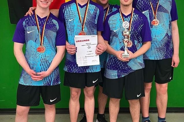 Vier Tischtennisspieler mit Medaillen und einer Urkunde stehen vor einer grünen Wand, lächeln in die Kamera.