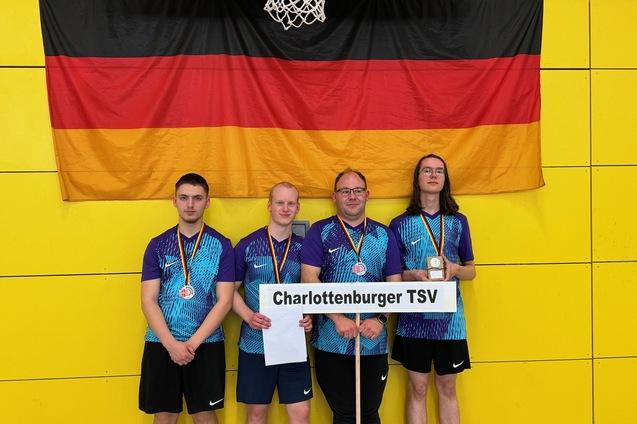 Vierte Spielergruppe des Charlottenburger TSV mit Medaillen, vor einer deutschen Flagge und gelbem Wandhintergrund.