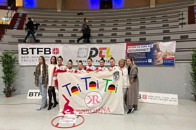 Gruppenshot mit sechs Tänzerinnen in roten Outfits und zwei Frauen, die ein Banner mit „Toi Toi Toi“ halten.