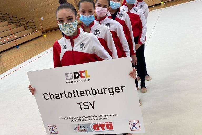 Sechs Tänzerinnen in roten und weißen Trainingsjacken stehen auf einer Matte und halten ein Schild mit „Charlottenburger TSV“.