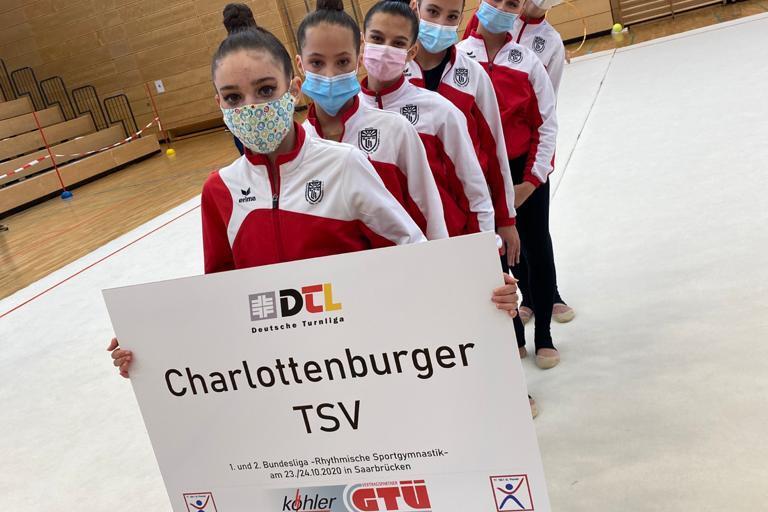 Sechs Tänzerinnen in roten und weißen Trainingsjacken stehen auf einer Matte und halten ein Schild mit „Charlottenburger TSV“.