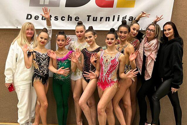Gruppe von Gymnastinnen in bunten Kostümen posiert vor einem Banner der Deutschen Turnliga.