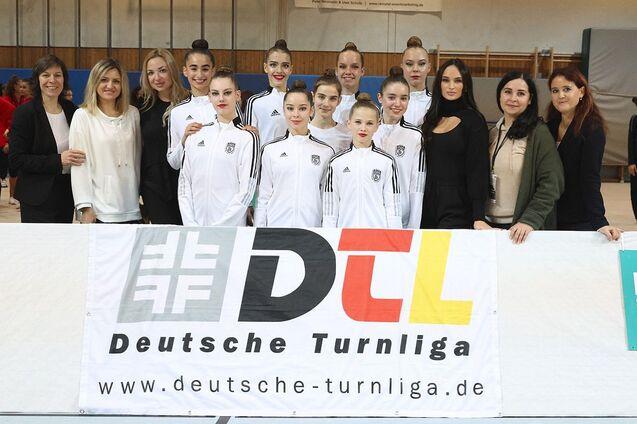 Gruppe von Tänzerinnen in weißen Sportanzügen vor einem Banner der Deutschen Turnliga.