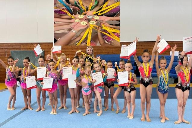Gruppe von Mädchen in bunten Kostümen halten Urkunden und Medaillen in einer Turnhalle.