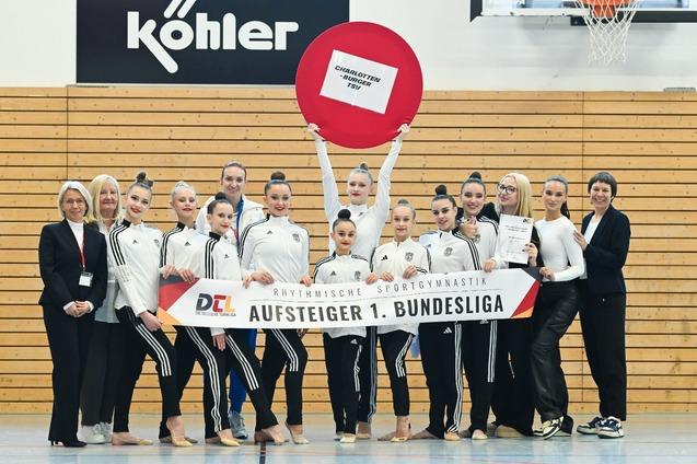 Gruppenfoto von Teammitgliedern der rhythmischen Sportgymnastik mit einem Banner „Aufsteiger 1. Bundesliga“ und einer Urkunde.