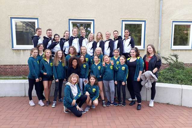 Gruppenfoto von Mädchen und Frauen in Sportbekleidung vor einer Wand, lächelnd und posierend für die Kamera.