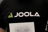 Mann mit Brille hält eine Urkunde in der Hand und trägt ein schwarzes T-Shirt mit dem Logo von JOOLA.