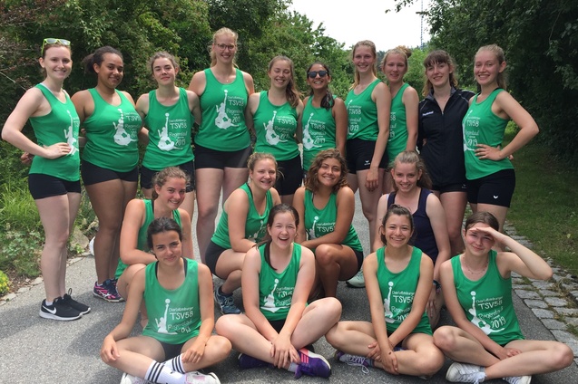 Gruppenfoto von 17 Sportlerinnen in grünen Trikots auf einem Weg, umgeben von Bäumen und Sträuchern.