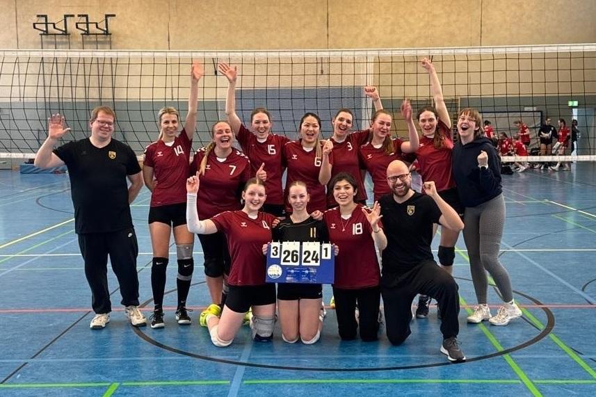 Volleyball-Team feiert den Sieg mit Punktestand 3:2, auf einem Spielfeld mit Netz im Hintergrund.