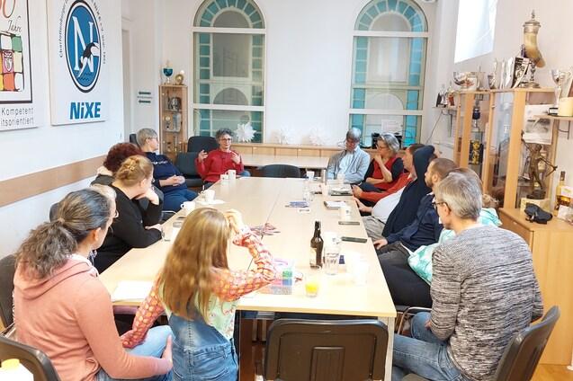 Eine Gruppenbesprechung mit mehreren Personen sitzt an einem langen Tisch in einem hellen Raum.