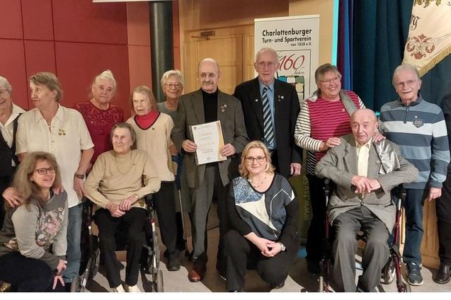 Gruppenfoto mit mehreren Erwachsenen, die an einer Ehrungsfeier teilnehmen, Urkunde in der Mitte eines Mannes.