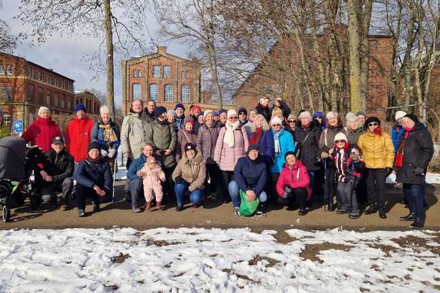 Gruppenfoto von 47 Personen in Winterkleidung, stehend und sitzend, vor einem Park mit schneebedecktem Boden.