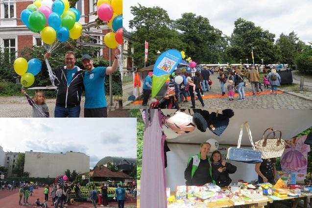 Menschen auf einem Fest halten Luftballons; Stände mit Spielen und Angeboten, viele Familien und Kinder im Hintergrund.