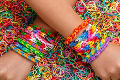 Bunte Gummibänder als Armbänder an beiden Handgelenken, umgeben von zahlreichen weiteren bunten Gummibändern.
