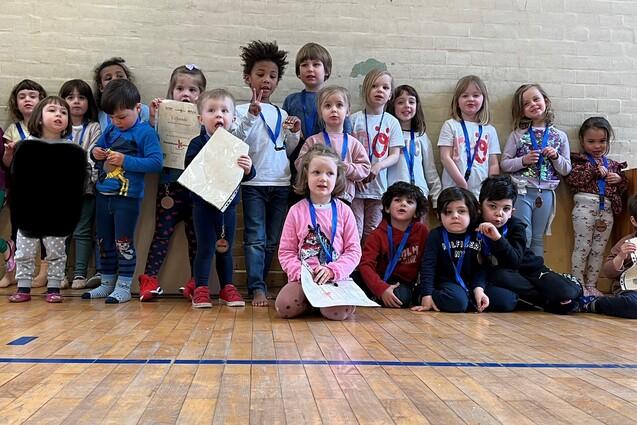 Gruppe von Kindern in Sportkleidung mit Medaillen und Urkunden, stehend vor einer Wand in einer Turnhalle.