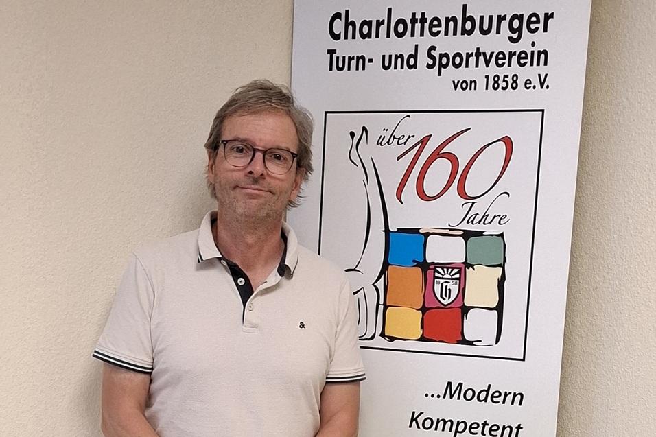Mann mit Brille steht neben einem Banner des Charlottenburger Turn- und Sportvereins, das 160 Jahre feiert.