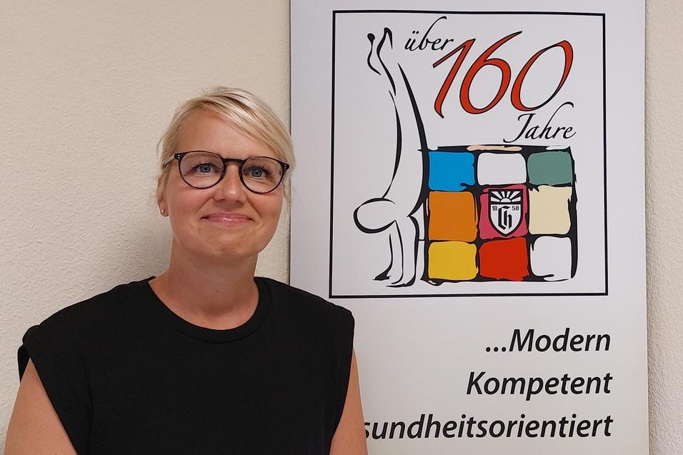 Frau mit blonden Haaren und Brille steht neben einem Banner des Charlottenburger Turn- und Sportvereins mit Logo und Slogan.