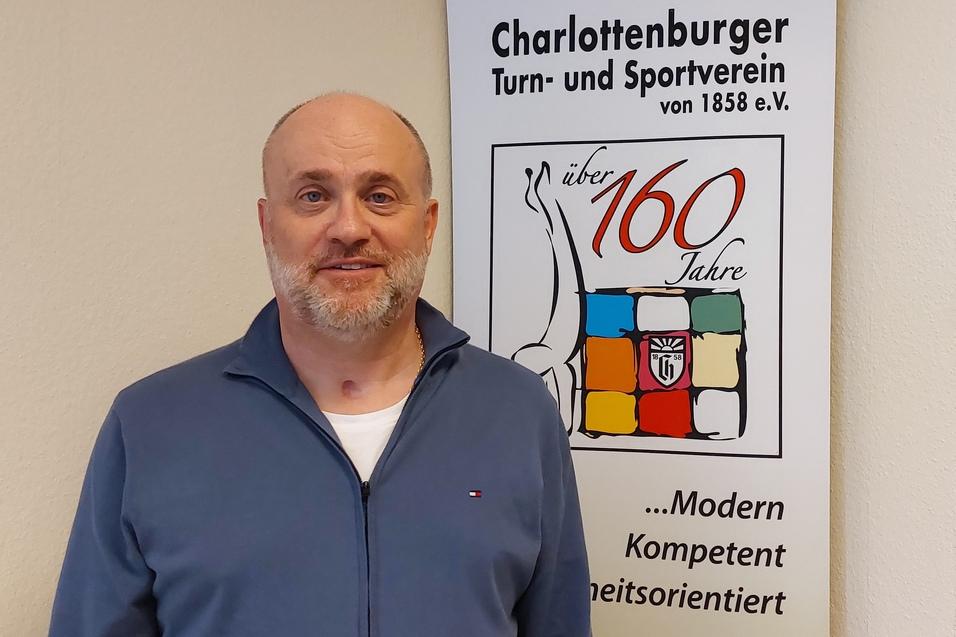 Mann mit kurzem Bart steht neben dem Banner des Charlottenburger Turn- und Sportvereins mit der Aufschrift „über 160 Jahre“.