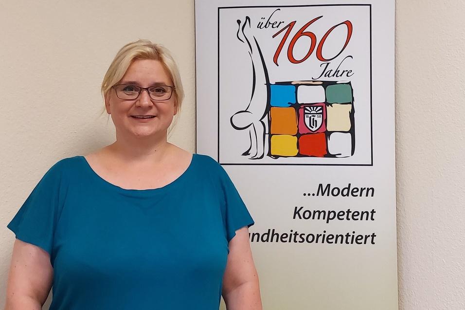 Frau mit blonden Haaren und Brille steht neben einem Banner des Charlottenburger Turn- und Sportvereins.