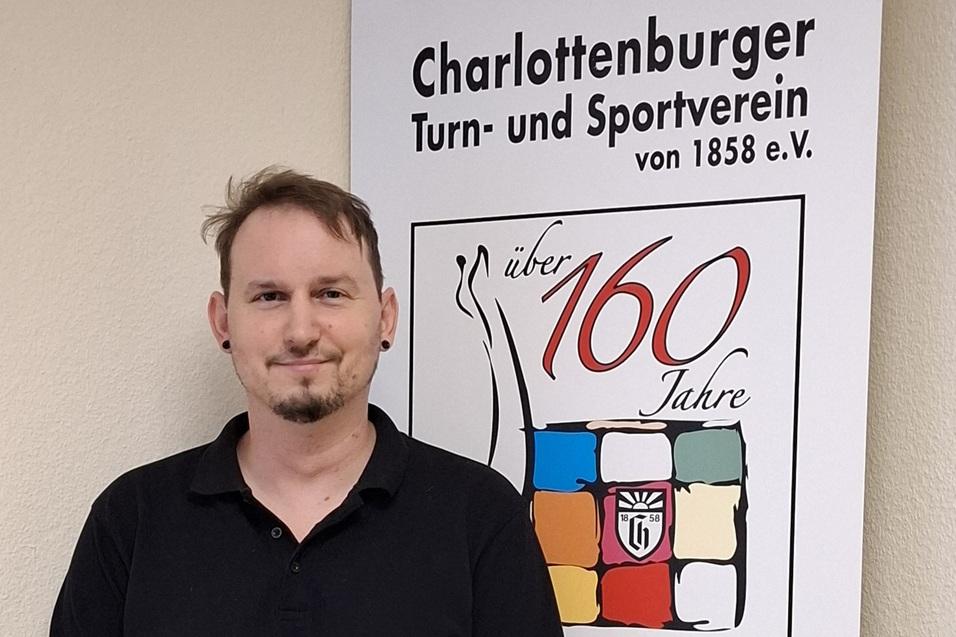 Mann mit Kurzhaarfrisur steht vor einem Banner des Charlottenburger Turn- und Sportvereins mit dem 160-Jahr-Logo.