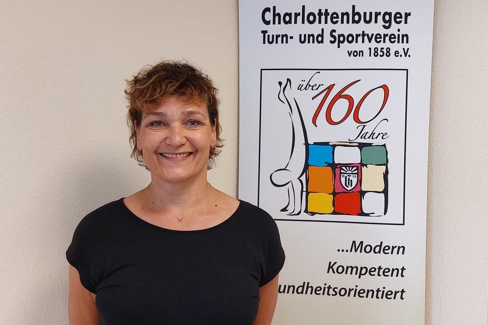 Frau mit lockigem Haar steht vor einem Banner des Charlottenburger Turn- und Sportvereins mit dem Logo und Slogan.