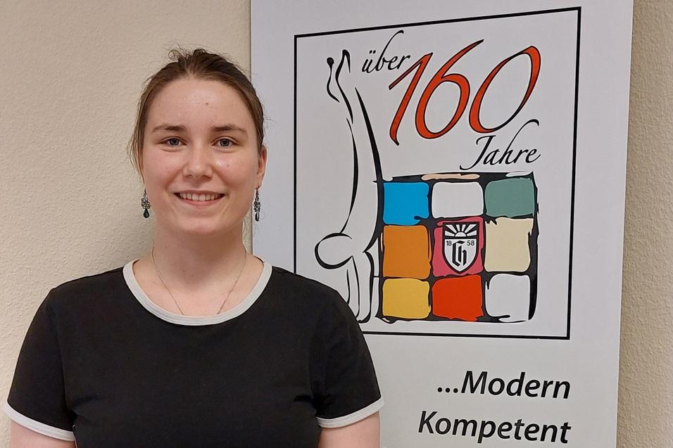 Frau mit einem schwarzen T-Shirt steht vor einem Banner des Charlottenburger Turn- und Sportvereins mit Jubiläumslogo.