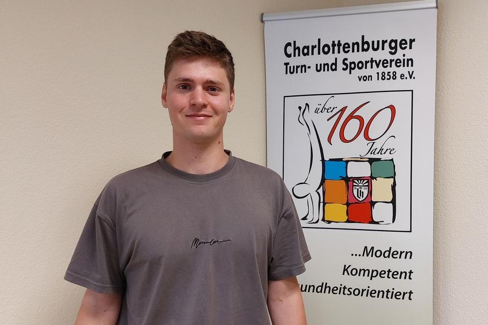 Junger Mann mit grauem T-Shirt steht vor einem Banner des Charlottenburger Turn- und Sportvereins.